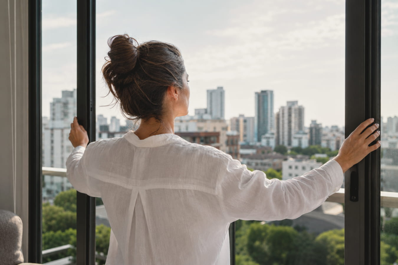 Mulher abrindo uma janela com vista para a cidade
